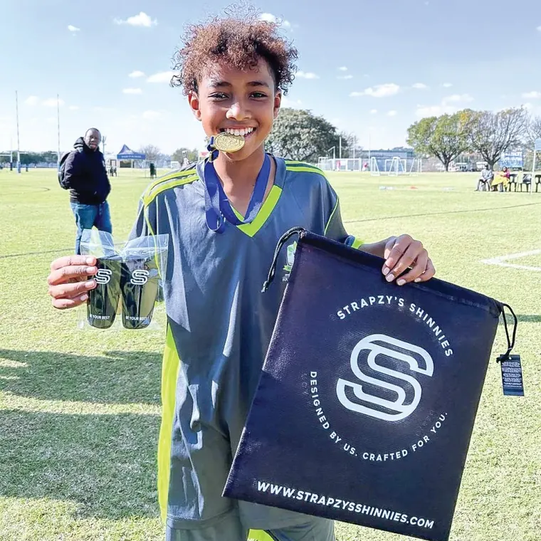 A young player holding their personalised shin pads and a Strapzy's gift bag